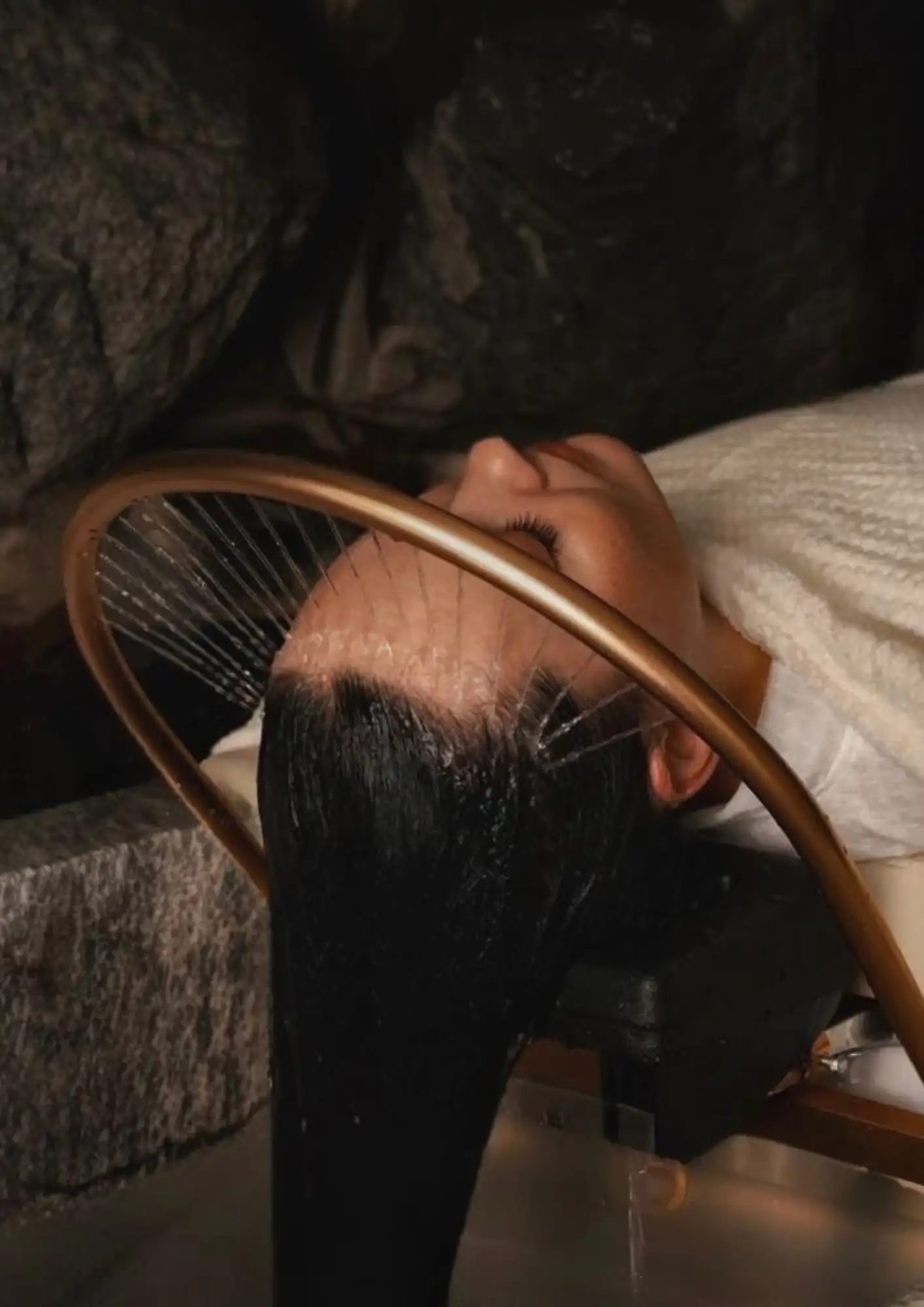 Cliente allongée pendant un head spa, la chevelure sous l'arche d'eau du bac de soin