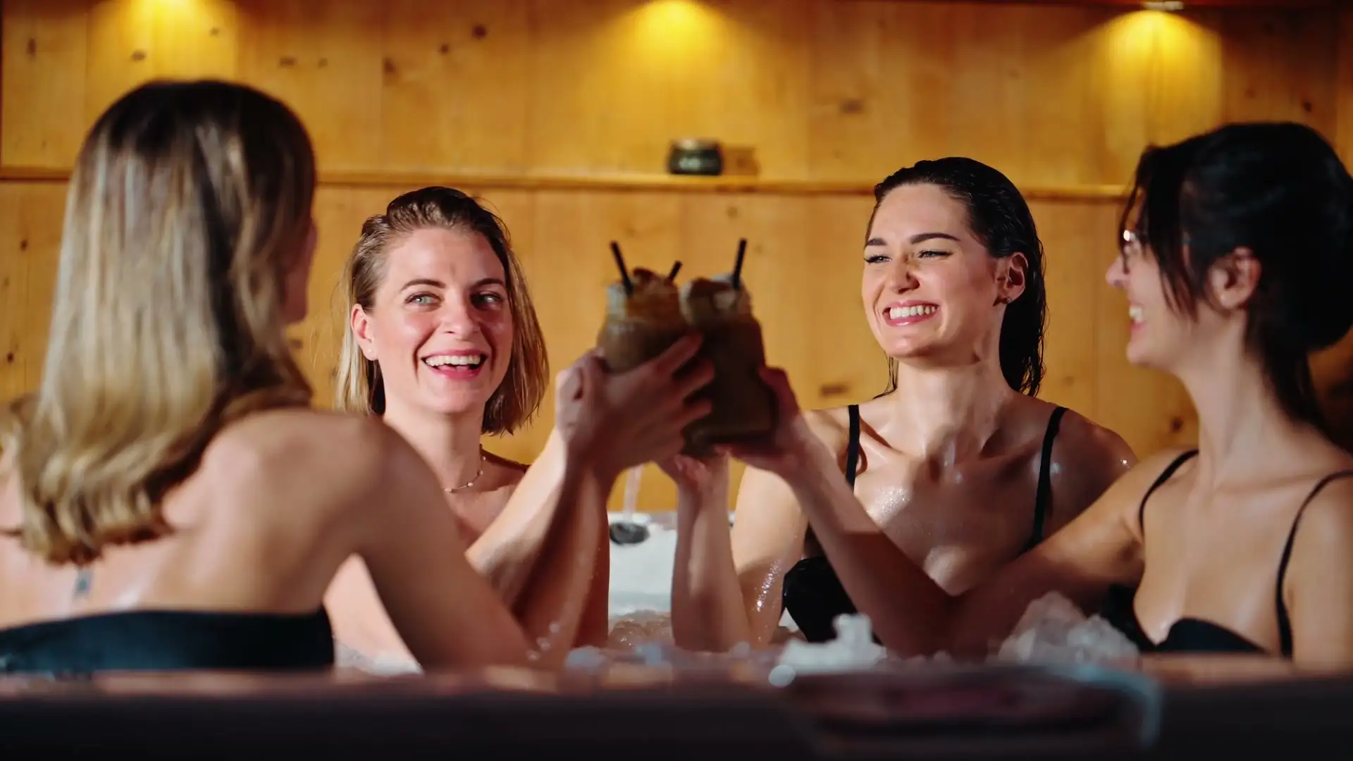 Quatre amies trinquent dans le spa à jets du Jardin d'Eden, sous une lumière chaude