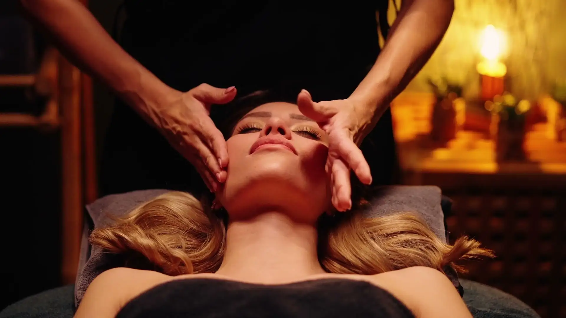 Modelage du visage d'une cliente allongée, à la lueur d'une bougie
