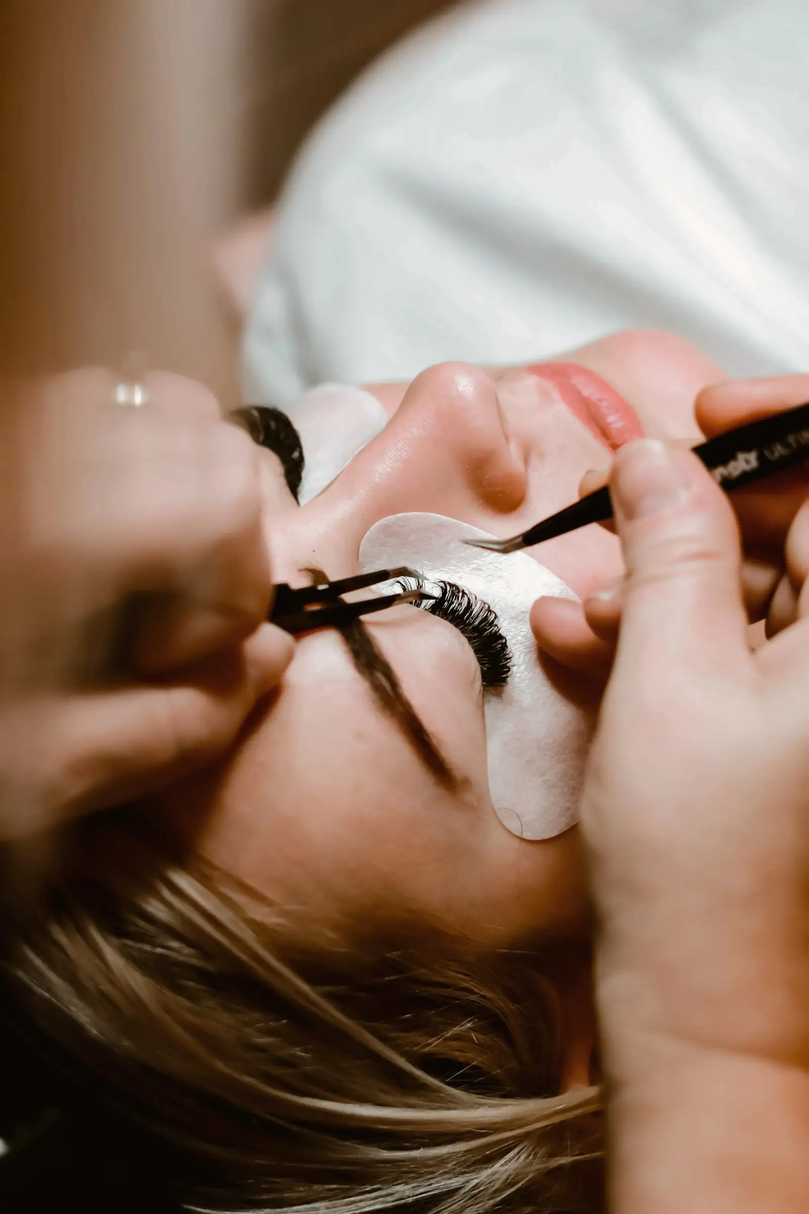 Pose d'extensions de cils à la pince, cliente allongée les yeux fermés
