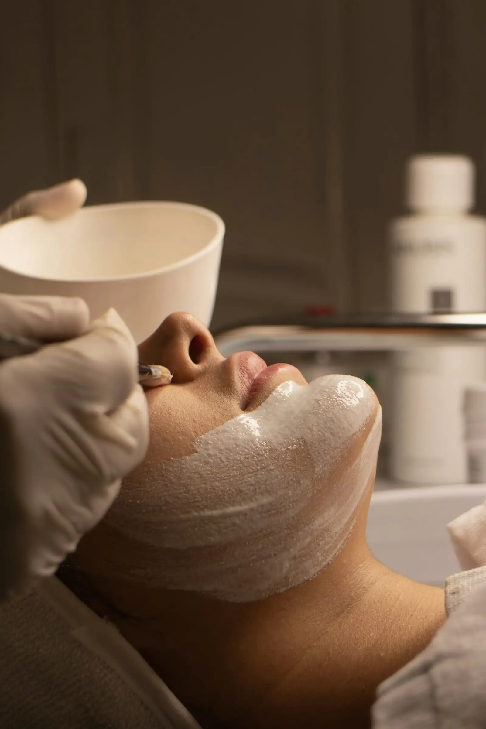 Soin du visage en cabine, masque appliqué par une esthéticienne gantée