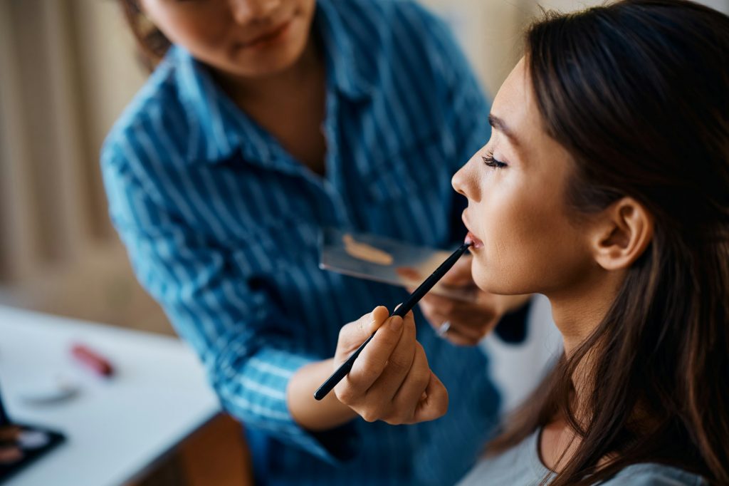 Close up of makeup artist applying lipstick with a brush on woman's lips.